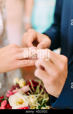 Groom`s hands are putting the wedding ring on the finger of the bride. Stock Photo